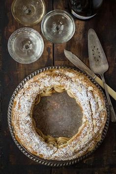 a table topped with a cake covered in powdered sugar next to wine glasses and utensils