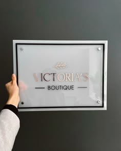 a person holding up a sign that says victoria's boutique in gold lettering on it