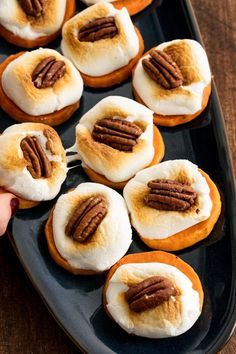 a tray filled with mini donuts covered in frosting and pecans on top