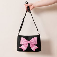 Jump into the pink bow aesthetic and coquette trend with this versatile pink bow crossbody bag with a black background. It has a modern and playful feel, which makes this handbag a great accessory and a perfect gift for every occasion. It's made of premium faux leather and features dark gray hardware. Thanks to the zip-top closure and multiple inside pockets, you can keep your essentials secure and organized. Transform this crossbody bag with removable wrist and shoulder straps to style it for d Pink Shoulder Bag With Bow For Everyday Use, Pink Shoulder Bag With Bow, Black Rectangular Bag With Bow, Pink Bow Bag For Daily Use, Black Bag With Detachable Bow, Black Party Bags With Bow Detail, Cute Black Shoulder Bag With Detachable Strap, Black Bow Shoulder Bag For Party, Cute Pink Bag With Bow