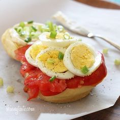 a sandwich with eggs, tomatoes and green onions on it sitting on top of a piece of paper