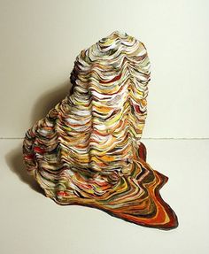 a sculpture made out of magazines sitting on top of a white table next to a wall