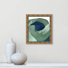 a white vase sitting on top of a table next to a framed art piece in a gold frame