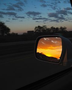 the sun is setting in the distance as seen from a car's rear view mirror