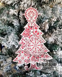 a paper cut christmas tree ornament hanging on a decorated christmas tree with red and white ornaments