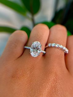 a woman's hand with a diamond ring on her finger and a plant in the background