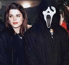 a woman standing next to a man in a black outfit with a scream mask on