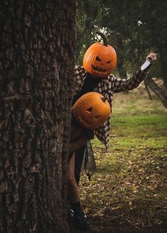 a woman holding two jack o lantern pumpkins on her head while standing next to a tree