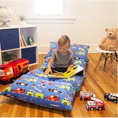 a young boy sitting on a bed reading a book in his room with toys around him