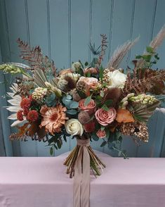 a bouquet of flowers sitting on top of a pink table cloth covered table with a blue wooden wall in the background