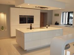 a modern kitchen with white cabinets and counter tops, along with an island in the middle