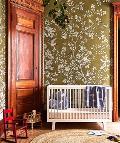 a white crib in front of a green wallpapered room with wooden doors