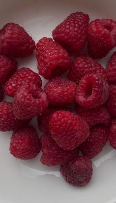 some raspberries are in a white bowl