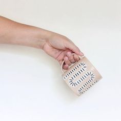 a hand holding a white and black ceramic mug with geometric designs on the inside, against a white background