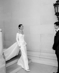 a man and woman standing next to each other in front of a light pole with a white dress on