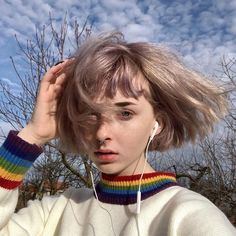 a woman with short hair wearing headphones in front of some trees and blue sky