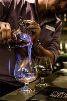 a man pours some liquid into two wine glasses