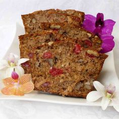 two slices of fruit and nut bread on a plate with orchids next to it