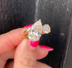 a woman's hand holding a yellow and white ring with two pear shaped diamonds