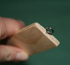 a person holding a piece of wood with a ring on it's end, in front of a green background