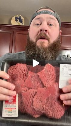 a man with a beard is holding up a tray of raw meat in front of him