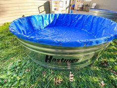 an empty metal tub sitting on top of green grass next to a house with a blue tarp over it