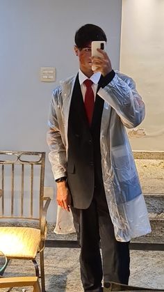 a man in a suit and tie taking a selfie with his cell phone while standing next to a chair