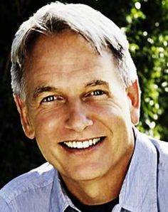 a close up of a person wearing a blue shirt and tie smiling at the camera