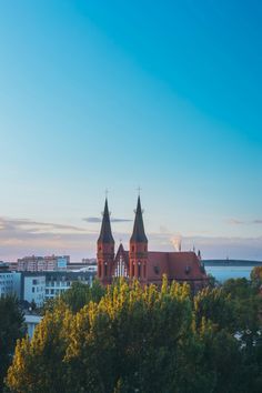 an image of a church in the middle of trees and buildings behind it with blue sky