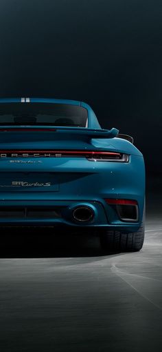 the rear end of a blue sports car in a dark room with its lights on