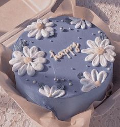 a blue cake decorated with white flowers and the words happy written on it in frosting