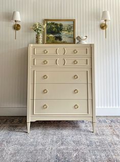 a white dresser sitting next to a wall with a painting on it's side