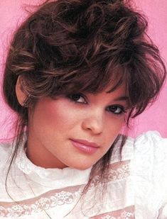 a close up of a person wearing a white shirt and hair in a bun with bangs