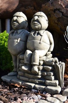 two stone statues sitting on top of a pile of rocks in front of a tree