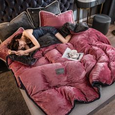 a woman laying on top of a bed covered in pink blankets and pillows, with a cup of coffee next to her