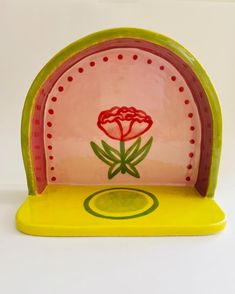 a pink and green plate with a red flower on the front, sitting on a yellow table