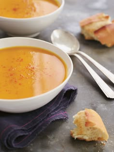 two white bowls filled with soup next to silver spoons on a gray counter top