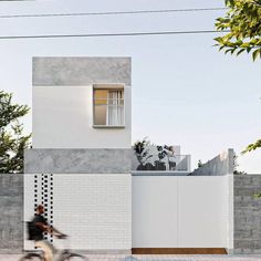 a person riding a bike in front of a white and grey building with a window