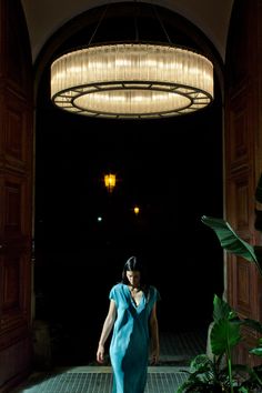 a woman in a blue dress is walking into a dark room with lights hanging from the ceiling