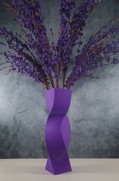 a vase with purple flowers in it sitting on a table next to a gray wall