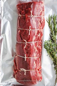 raw meat sitting on top of a piece of paper next to a sprig of rosemary