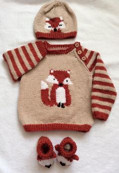 a knitted sweater, hat and booties are laying on a white sheet in the shape of a fox