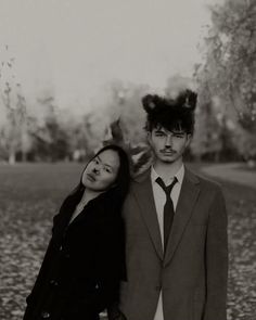 a man and woman standing next to each other in front of a field with trees