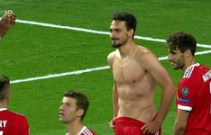 a man without a shirt standing on a soccer field with other men in red uniforms