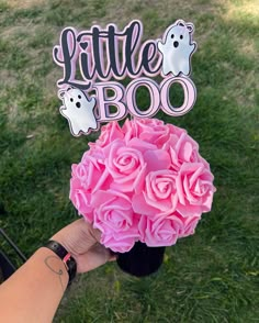 a person holding a bouquet of pink roses in front of a sign that says little boo