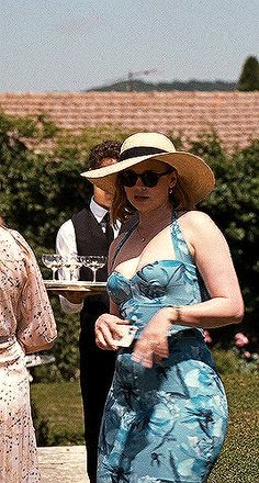 a woman in a blue dress and hat holding a tray with food on it while standing next to another woman