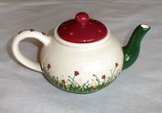 a ceramic teapot with a red lid and flowered design on the outside, sitting on a white surface