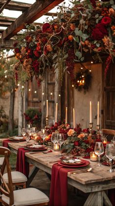 an outdoor dining table with candles and flowers on the top, surrounded by greenery