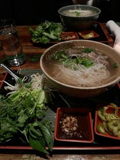 a wooden table topped with bowls filled with soup and veggies on top of it