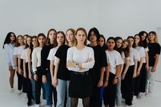 a group of women standing next to each other in front of a white wall with their arms crossed